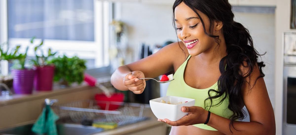 Cheerful woman enjoying fresh strawberries in a cozy kitchen setting. Promotes healthy living and happiness.