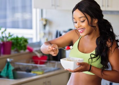 Cheerful woman enjoying fresh strawberries in a cozy kitchen setting. Promotes healthy living and happiness.